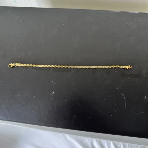 Guldarmband med tvinnad kedja - Snyggt armband i guld med tvinnad kedja och klassiskt spänne. Perfekt accessoar för att lyfta din stil med en elegant touch. Passar både till klocka eller andra smycken för en trendig look.
