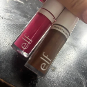 e.l.f. bronzer & läppglans duo - Två sminkprodukter från e.l.f.: ett flytande bronzer & contour i en varm brun nyans och ett läppglans i en starkt rosa färg. Båda kommer i smidiga tuber med vita lock och genomskinlig botten som visar färgen tydligt. Perfekt för att skapa en fräsch look.