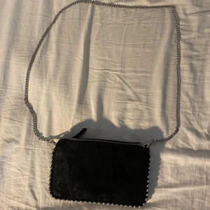 Svart axelväska med kedja från Zara - Snygg svart axelväska från Zara i mocka med silverfärgad kedja som axelrem. Väskan har dragkedja upptill och coola silverkulor längs kanterna som ger en edgy vibe. Perfekt storlek för det viktigaste och passar till många olika outfits.