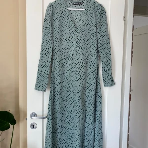Lång prickig klänning från Missguided - Ljusgrön supersöt långklänning från Missguided med svarta prickar, v-ringning och knappar framtill. I storlek 38. Använd ett fåtal gånger. 