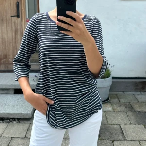 Randig marinblå tröja med trekvartsärm - Snygg marinblå och vitrandig tröja med trekvartsärmar och rund halsringning. Tröjan har en avslappnad passform och är gjord i mjuk bomull, perfekt för en chill och stilren look. Passar lika bra till jeans som till shorts.