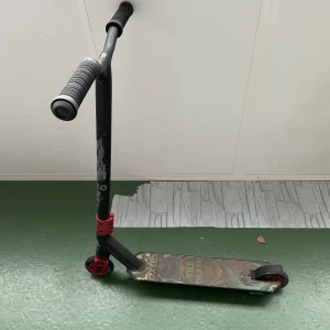 Oxelo trick sparkcykel  - Bilderna visar en sparkcykel av märket Oxelo med coolt motiv och texten 'Till Death' på decket. Den har röda hjul och detaljer, samt robusta handtag. Perfekt för dig som gillar att cruisa eller göra tricks med stil. Snygg design som sticker ut på skateparken.