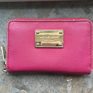Rosa Michael Kors Plånbok - Snygg rosa plånbok från Michael Kors med guldfärgad logoplatta framtill. Plånboken har dragkedja runtom och flera fack för kort och sedlar. Perfekt storlek för att ha med sig överallt. Kontakta om fler frågor uppstår, priset går att diskutera.