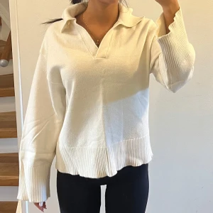 Vit stickad tröja med krage - Säljer en vit stickad tröja med breda ribbade muddar och krage. Tröjan har v-ringad öppning framtill och långa ärmar med extra vida avslut. Perfekt för dig som gillar en chill och stilren look.