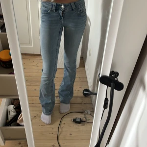 Ljusblå bootcut jeans med fickdetalj - Snygga ljusblå jeans med bootcut passform och klassisk femficksdesign. Jeansen har en knappdetalj på bakfickan och är tillverkade i mjukt denimtyg. Perfekta för dig som gillar en avslappnad men ändå trendig look.