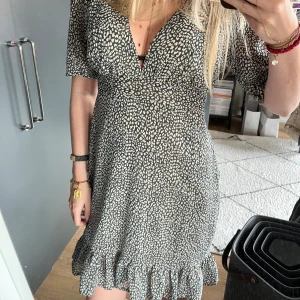 Mönstrad kortklänning från Jane Wood - Supersöt kortklänning från Jane Wood med blå/grön och vit leopardmönster, v-ringning och volangkant nertill. Klänningen har korta ärmar och markerad midja