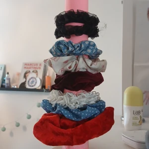 Mixade scrunchies i olika färger - Säljer ett gäng scrunchies i olika material och färger: svart volang, blå med blommor, vit med hjärtan, vinröd sammet, vit spets, blå med prickar och röd sammet. Perfekt för att piffa upp håret med olika stilar! 15 kr st