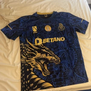 FC Porto special tröja - Snygg FC Porto fotbollströja i mörkblått med gult drakmotiv och detaljer. Kortärmad modell med klubbmärke, sponsortryck och coolt mönster över hela framsidan. Tillverkad i lätt och ventilerande material, perfekt för match eller träning. Obs lite liten i storlek