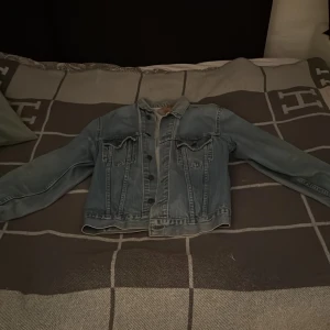 Klassisk blå jeansjacka från Levi's - Säljer en klassisk blå jeansjacka från Levi's med snygga bruna knappar och två bröstfickor med lock. Perfekt att ha över en hoodie eller t-shirt. Tveka inte på att höra av er om ni har fler frågor!🤝