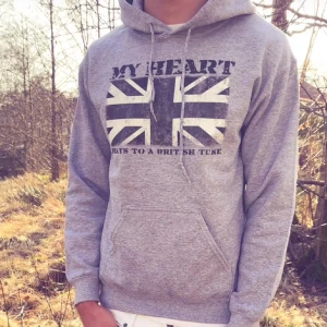 Grå hoodie med brittisk flagga - Helt NY grå hoodie i storlek L men passar M med tryck av Union Jack och texten 'MY HEART BEATS TO A BRITISH TUNE' på bröstet. Klassisk känguruficka, snörning i huvan och mjukt material. Perfekt för dig som gillar streetstyle och brittisk vibe.