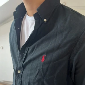 Ralph Lauren Skjorta Slimfit  - Säljer en svart Ralph Lauren skjorta i Slimfit/normalfit. Jätte bra skick. Då de är en gammal model står de storlek 20 Men det motsvarar en M ! Riktigt fräsch till sommaren och för ett sånt bra pris går de inte fel! Fraktar samma dag !! 