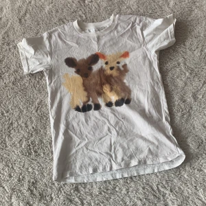Vit t-shirt Rop van Mierlo x H&M - Vit t-shirt från Rop van Mierlo x H&M med ett gulligt tryck av två djur på framsidan. Klassisk rund hals och korta ärmar. Tillverkad i mjuk bomull, perfekt för en chill och lekfull stil.