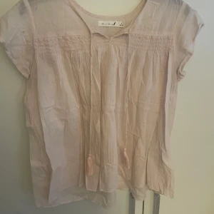 Ljusrosa blus från Black Story - Supersöt ljusrosa blus från Black Story med korta ärmar och knytband med tofsar framtill. 