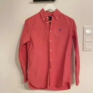 Ralph lauren skjorta - Säljer denna sjukt snygga röd/rosa Raffe skjortan som passar perfekt till sommaren, skjortan är använd med i gott skick! Storlek XS. Nypris ligger på 1600kr+! Vid fler frågor är det bara att höra av sig.