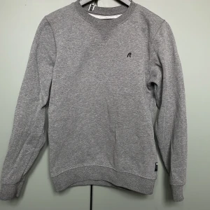 Grå sweatshirt från Replay - En stilren grå sweatshirt från Replay med broderad svart R-logga på bröstet. Tröjan har rund halsringning, ribbade muddar och är tillverkad i mjuk bomullsmix. Perfekt för dig som gillar en clean och enkel look.