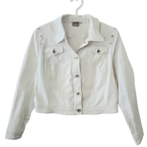  Off-white jacka med silvriga knappar - Snygg off-white jeansjacka med silvriga knappar och detaljer på axlarna. Klassisk krage, två bröstfickor med lock och knapp samt långa ärmar. Perfekt att slänga över en hoodie eller t-shirt för en clean look. Jackan ser mindre ut men passar storlek M-L istället för XL.