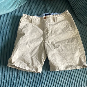 Beige shorts från Gant, 13-14 år - Snygga beige shorts från Gant med klassisk passform och bälteshällor. De har två sidofickor fram och två bakfickor med knapp. Tillverkade i mjuk bomull, perfekta för varma dagar. Stilsäkra och enkla att matcha med det mesta.