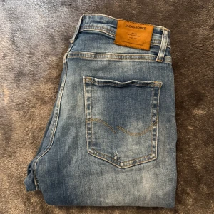 Jack & Jones jeans  - Säljer ett par ljusblå jeans från Jack & Jones med snyggt tvättad look och klassiska fem fickor. Modellen är tapered med normal passform och orangea kontrastsömmar. Perfekta för en avslappnad stil och funkar året runt. 