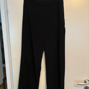 Svarta wide byxor från BikBok - Svarta byxor från BikBok i storlek 40. De har en hög midja och vida ben för en chill och trendig look. Byxorna är gjorda i ett mjukt och lätt material som känns skönt mot huden. Perfekta att styla med crop top eller oversized hoodie.