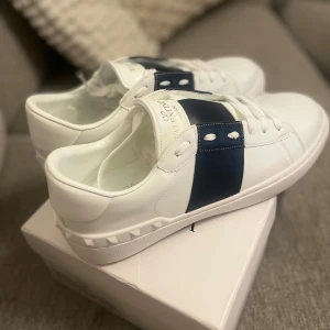 Valentino Garavani sneakers vit/blå - Snygga vita Valentino Garavani sneakers med bred marinblå rem över mitten. Helt nya, aldrig använda vilket syns på bild med. Säljer de pågrund av att de var för små🙌