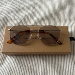Solglasögon Corlin Eyewear - Snygga solglasögon från Corlin Eyewear med silvriga metallbågar och fyrkantig form. Glasen är mörktonade och skalmarna har en brunskiftande sköldpaddsmönstrad look 🤎