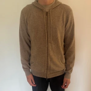Davids beige hoodie i kashmir  - Beige hoodie från Davida i 100% kashmir. Tröjan har dragkedja framtill, huva med snören och två fickor. Fint skick, sparsamt använd.