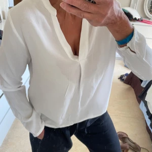 Blus  från 365, stl 40 - Snygg vit blus  från 365 med v-ringning och lång ärm. Skjortan har en avslappnad passform och är tillverkad i ett lätt, vävt tyg som känns luftigt. Perfekt till jeans eller kostymbyxor för en clean look.