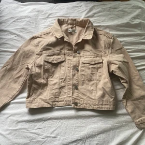 Beige jeansjacka  - Snygg beige jeansjacka från gina i klassisk modell med krage, knappar framtill och två bröstfickor. Jackan är croppad och har långa ärmar. Den är ganska flitigt använd men fortfarande i bra skick. Den är i storlek M men är ganska liten i storleken så passar S