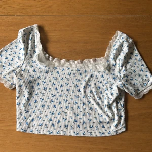 Vit blommig croppad blus med spets - Supersöt croppad blus i vit med blått blommönster och tunna svarta ränder❣️ Strl L helt ny!!❣️