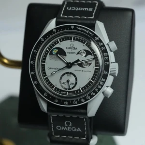 Förbästella Omega x Swatch MoonSwatch Speedmaster - Omega x Swatch MoonSwatch Speedmaster med svart och silver urtavla, tachymeter och lysande visare. Klockan har svart textilband med vit söm och Omega-logga. Snygg och futuristisk design med månmotiv på urtavlan. Perfekt för dig som gillar rymdtema och coola detaljer. Jag har beställt det, och leveransen kommer att vara sen