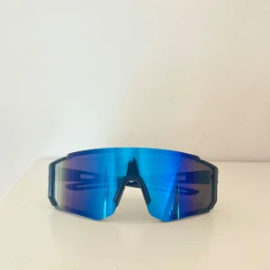 Snygga sportiga solglasögon  - Säljer ett par sportiga solglasögon med spegelblått, stort shield-glas och svarta skalmar. Glasögonen har en futuristisk vibe med kantig form och bred täckning, perfekta för dig som gillar att sticka ut🤵🏼Lätta och bekväma för aktiva dagar utomhus😎