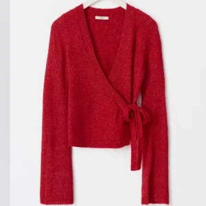 Röd omlottkofta med knyt - Säljer en röd stickad omlottkofta med knyt i sidan från Gina tricot. Tröjan har långa ärmar och en croppad passform. Perfekt för lager-på-lager och ger en snygg siluett. Supermjuk och skön att bära.(oanvänd)