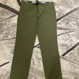 Olivgröna chinos från Polo Ralph Lauren - Säljer ett par olivgröna chinos från Polo Ralph Lauren. Byxorna har slim fit passform och är stretchiga för extra komfort. Klassisk design med knäppning och fickor, perfekta för en stilren look.