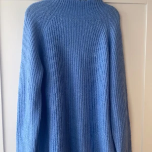Blå ribbstickad tröja med hög krage - Säljer en blå ribbstickad tröja med lång ärm och hög krage. Tröjan har en klassisk, rak passform och är perfekt för kyligare dagar. Enkel och stilren design som passar till mycket.