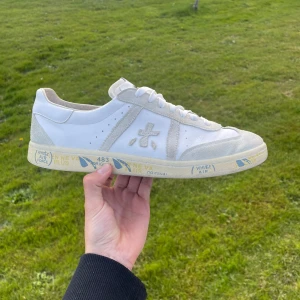Premiata skor - Säljer ett par vita sneakers från Premiata med beige detaljer och snörning. Jätte bra skick och snygga till sommaren! Box och dust bag medföljer! Skriv vid minsta lilla pris förslag eller fundering!