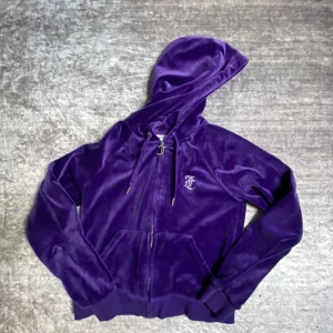 Lila velour hoodie från Juicy Couture - Juicy Couture hoodie i lila velour med dragkedja och huva. Tröjan har glittrande JC-logga på ryggen och metall-detaljer på snörena. Perfekt för en avslappnad och trendig look. Lägger även ut denna för 700 men är ni sugna på att köpa både den lila o bruna så lägger ja ut båda för 1300
