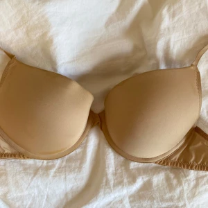 Beige bh från H&M - Säljer en beige bh från H&M med släta kupor och justerbara axelband. Bh:n är tillverkad i en mjuk och stretchig polyamidblandning och passar perfekt under ljusa plagg. Den har brun utan sol fläckar men tvättar den så kommer det gå bort 