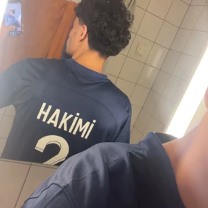 PSG Hakimi tröja - Säljer en mörkblå Paris Saint-Germain fotbollströja med Hakimi och nummer 2 på ryggen. Tröjan har vita och röda detaljer, PSG-logga och Qatar Airways som sponsor på bröstet. Klassisk kortärmad modell.