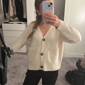 Vit kofta från Vero Moda - Mysig vit kofta från Vero Moda med stora knappar framtill och två fickor. Koftan har lång ärm och är ribbad vid ärmslut och nederkant. Perfekt att slänga på sig när det är lite kyligt ute .