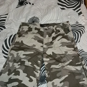 Cargoshorts med camouflage från Stuff - Säljer ett par cargoshortsr i grått och beige camouflage från Stuff. Byxorna har flera fickor, dragkedja i sidan och klassisk cargomodell. Perfekta för dig som gillar streetstyle eller vill ha något bekvämt och snyggt.