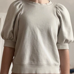 Beige sweatshirt med puffärmar - Säljer en beige sweatshirt med korta puffärmar och rund halsringning. Tröjan har en avslappnad passform och är gjord i mjukt bomullsmaterial. Perfekt för en trendig vardagslook.