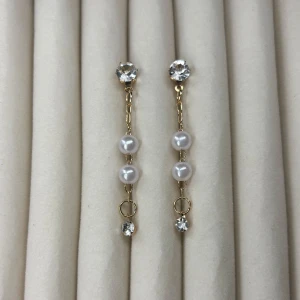 Guldiga örhängen med pärlor och stenar - Säljer ett par eleganta örhängen i guldton med två vita pärlor och gnistrande stenar. Perfekta för att lyfta din look med en touch av glamour. Lätta att bära och passar till många stilar.