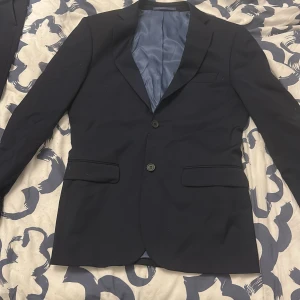 Mörkblå kostym från Dressmann - Säljer en stilren mörkblå kostym från Dressmann i slim fit-modell. Kavajen är i strl 44, byxorna 30/30, det medföljer även en vit dressmann kostymskjorta i strl 37/38. Kostymen är använd 2 gånger. Allting stryks innan det skickas, hör av er om ni är intresserade😌