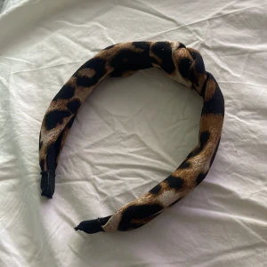 Leopard hårband - Snyggt diadem med leopardmönster i bruna, svarta och beige toner. Diademet har en twistad detalj upptill och är perfekt för att ge en trendig touch till din look.