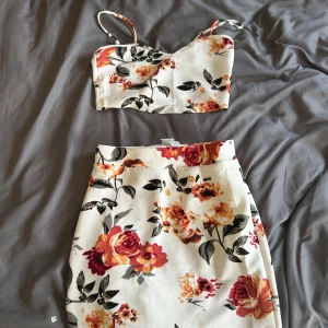 Blommig croppad linnetopp från SHEIN - Säljer en vit croppad linne och en kjol från SHEIN med färgglatt blommönster i rött, orange och gult. Toppen har smala axelband och en hjärtformad urringning. Perfekt för varma dagar och somriga outfits!den är aldrig använd heller 