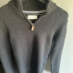 Svart stickad half zip från pier one - Svart stickad tröja från Pier One med hög krage och dragkedja framtill. Tröjan har långa ärmar och ribbade detaljer vid krage, ärmslut och nederkant. Perfekt för kyligare dagar.