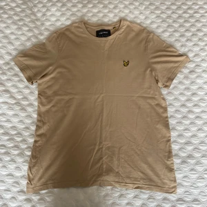 Beige t-shirt från Lyle & Scott - Säljer en beige t-shirt från Lyle & Scott med klassisk gul broderad logga på bröstet. T-shirten har rund halsringning och korta ärmar. T-shirten har knappt använts och är i mycket bra skick. Storlek: M