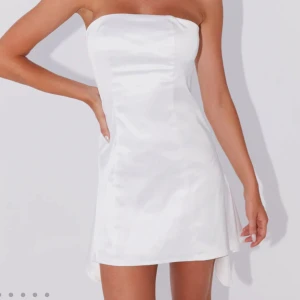 Vit bandou satin klänning från Peppermayo - Säljer en vit axelbandslös kortklänning i satin från Peppermayo. Klänningen har en enkel och stilren design med lätt figurnära passform och slät yta som ger en lyxig känsla. Perfekt för dig som gillar minimalistisk stil. (Säljer då den var något kort för min smak, är 166cm. Perfekt till studentklänning och är oanvänd med prislapp kvar)