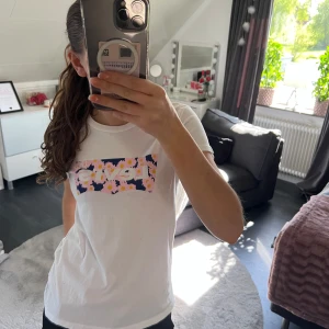 Vit t-shirt med blommigt Levi's-tryck - Vit t-shirt från Levi's med ett färgglatt blommigt tryck i rosa, gult och blått på bröstet. Klassisk passform och rund halsringning. Perfekt för dig som gillar en enkel men ändå lekfull stil.