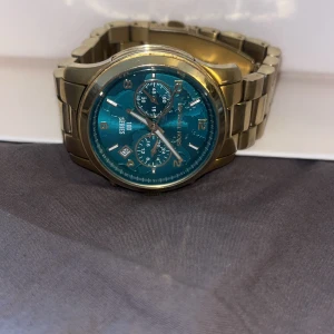 Guldig Michael Kors herrklocka med blå urtavla - Snygg herrklocka från Michael Kors i guldigt metallarmband och blå urtavla. Klockan har kronograf-funktion, datumvisning och tydliga siffror. Perfekt accessoar för dig som vill sticka ut med stil. Lådan är slängd och kvittot också